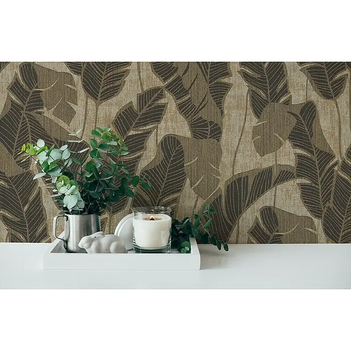 A.S. Création Jade 2 Vliestapete Blätter - Schwarzbeige, Floral, 10,05 x 0,53 m - Zimmerdekoration mit tropischem Blätter-Motiv, einem silbernen Krug mit Eukalyptus, einer Kerze und einer Hasenfigur auf einem weißen Tablett.