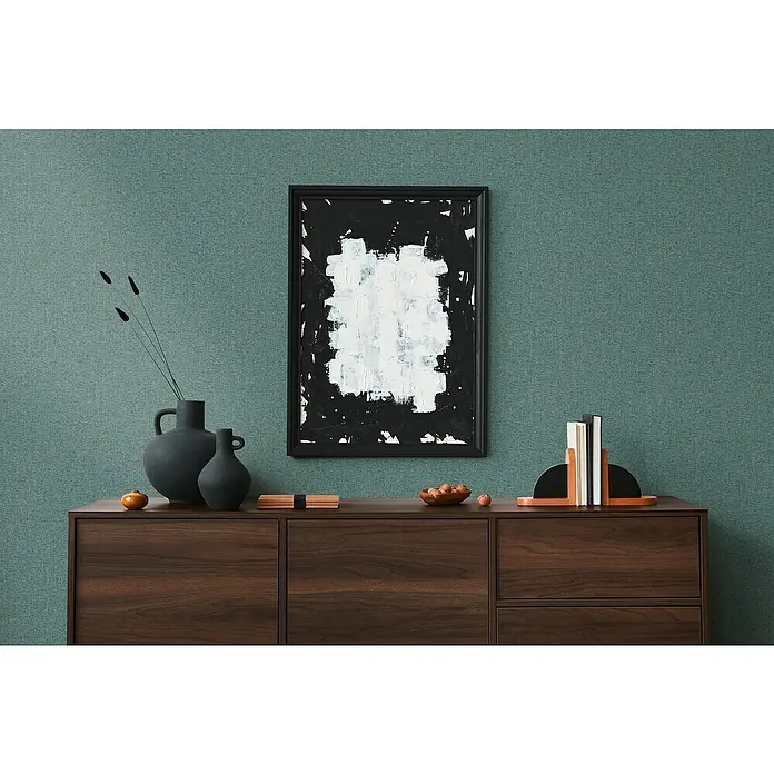 A.S. Création Famous Garden Vliestapete - Petrolblau, Uni, 10,05 x 0,53 m - Elegantes Sideboard aus dunklem Holz mit Deko-Objekten, darunter Vasen, Bücherstützen und ein abstraktes Kunstwerk an der Wand.