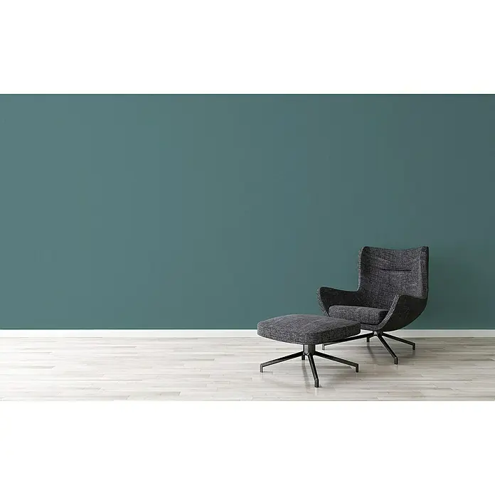 A.S. Création Jade 2 Vliestapete - Grün-Blau, Uni, 10,05 x 0,53 m - Ein moderner Sessel mit passendem Hocker in einem minimalistischen Raum, der Komfort und Stil vereint. Der Sessel lädt zum Entspannen ein.