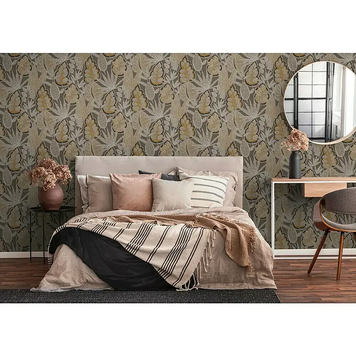 A.S. Création Famous Garden Vliestapete Blatt - Braun-Orange-Weiß, Floral, 10,05 x 0,53 m - Schlafzimmer mit floral gemusterter Tapete, Bett mit Kissen und Decken, Beistelltisch und Schreibtisch mit Spiegel und Stuhl.