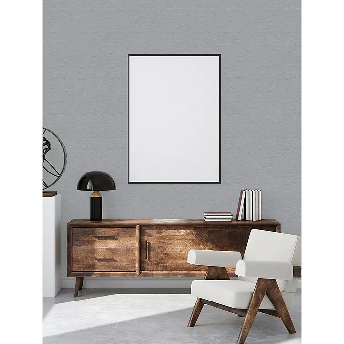 A.S. Création Famous Garden Vliestapete - Mittelgrau, Uni, 10,05 x 0,53 m - Das Bild zeigt ein modernes Wohnzimmer mit einem Holzschrank, einem Sessel und einem gerahmten Bild an der Wand. Die Einrichtung ist stilvoll und einladend.