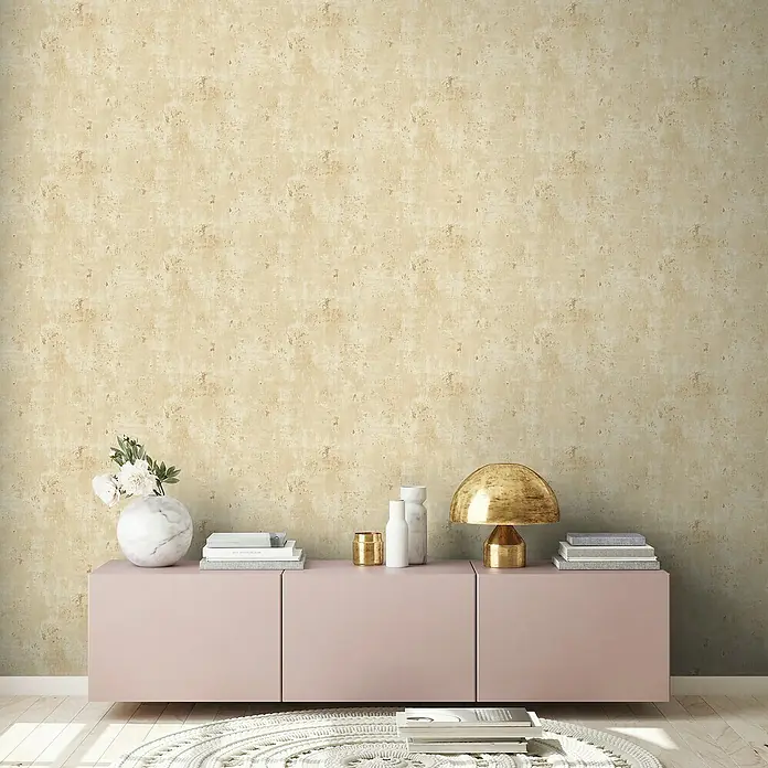 A.S. Création Stories of Life Vliestapete Patina - Beige-Gold, Betonoptik, 10,05 x 0,53 m - Einrichtungsidee mit einer rosa Kommode, einer goldenen Lampe und dekorativen Accessoires vor einer strukturierten Wand.