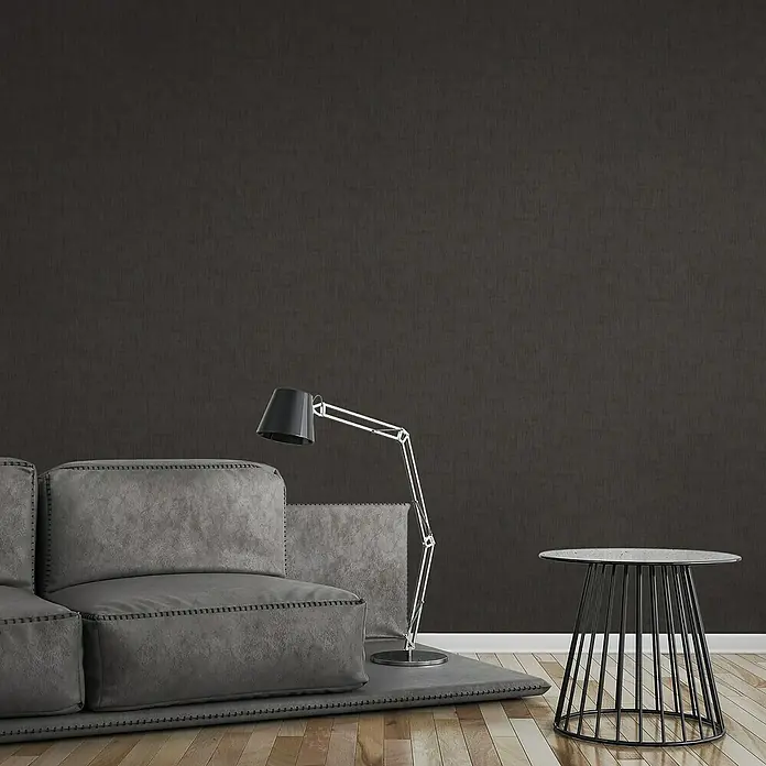 A.S. Création Jade 2 Vliestapete - Schwarz, Uni, 10,05 x 0,53 m - Eine moderne Wohnzene mit einem grauen Sofa, einer Stehlampe und einem Beistelltisch. Der dunkle Hintergrund sorgt für eine elegante Atmosphäre.