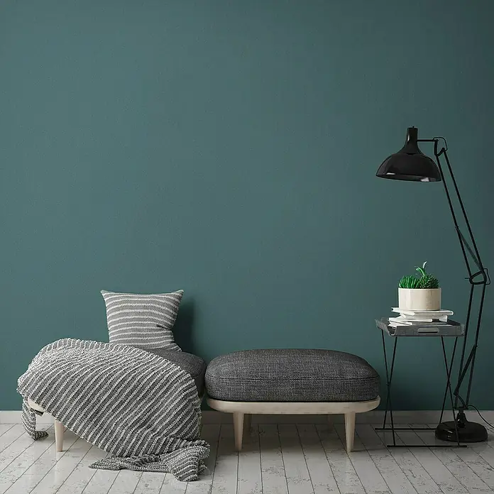 A.S. Création Jade 2 Vliestapete - Grün-Blau, Uni, 10,05 x 0,53 m - Gemütlicher Wohnbereich mit grau gestreiftem Überwurf und Kissen auf einer Bank, ergänzt durch einen passenden Hocker und eine Stehlampe mit Beistelltisch.