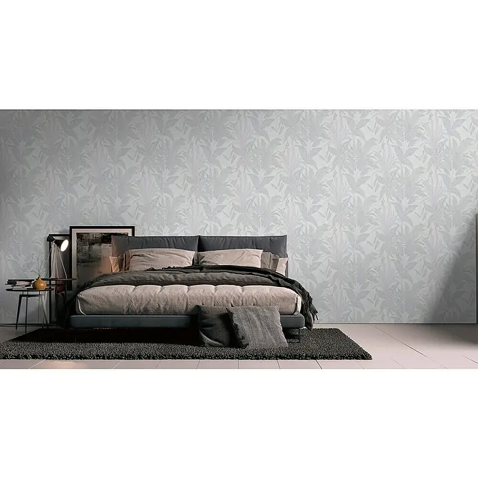 A.S. Création Stories of Life Vliestapete Dschungel - Grau-Creme-Gold, Floral, 10,05 x 0,53 m - Elegantes Schlafzimmer mit einem Bett mit graublauem Rahmen, beige Kissen und einer dunklen Decke vor einer Tapete mit Pflanzenmuster.