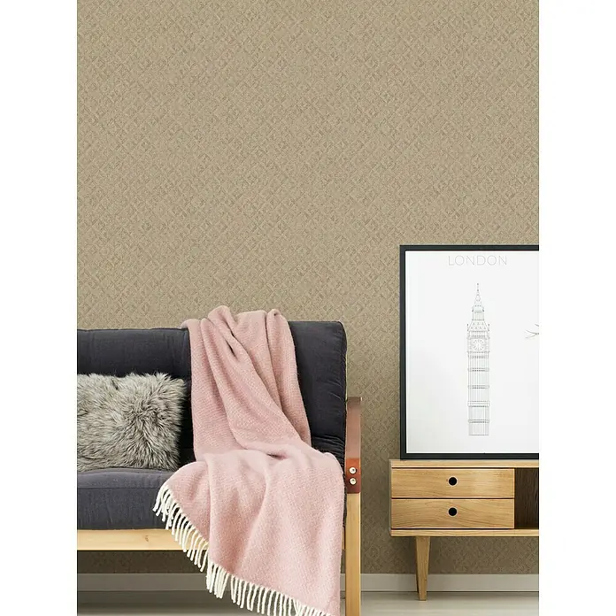 A.S. Création Jade 2 Vliestapete - Beige-Gold, Grafisch, 10,05 x 0,53 m - Wohnzimmer-Szene mit bequemer Couch, flauschigem Kissen und weicher Decke vor einer strukturierten Wand. Ein London-Poster steht auf einem Nachttisch.