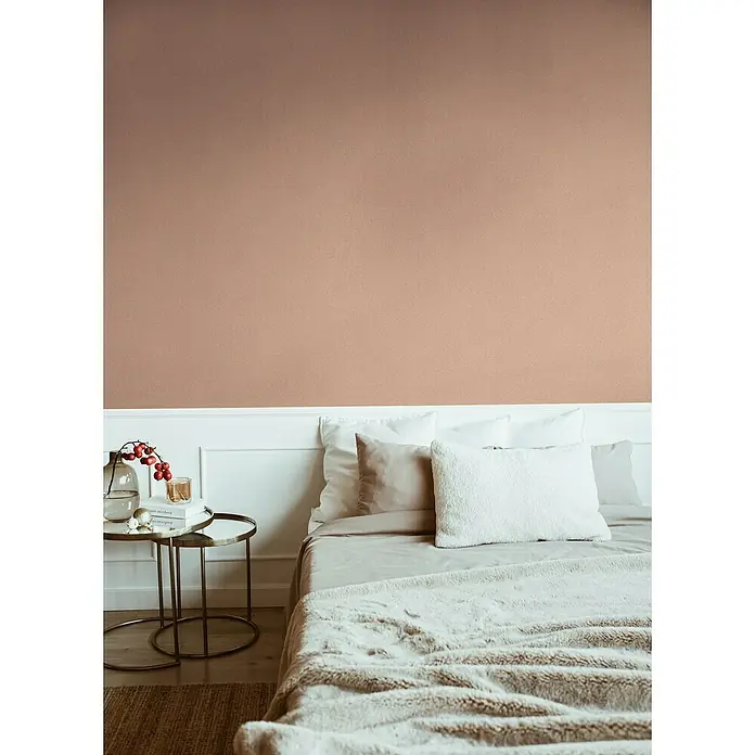 A.S. Création Jade 2 Vliestapete - Rosa-Orange, Uni, 10,05 x 0,53 m - Elegantes Schlafzimmer mit einem bequemen Bett mit flauschiger Decke und dekorativen Kissen vor einer stilvollen Wand.