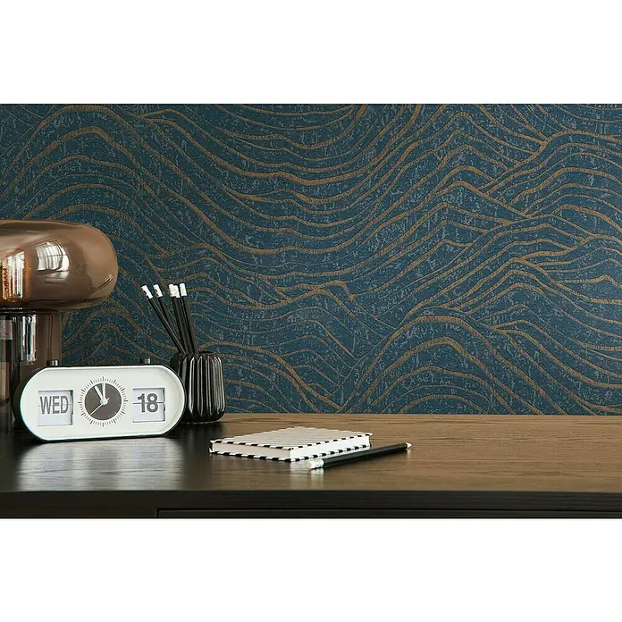 A.S. Création Jade 2 Vliestapete - Dunkelblau-Gold, 3D-Optik, 10,05 x 0,53 m - Stilvoller Schreibtisch mit Flip-Uhr, Lampe, Stiften und Notizbuch vor einer blauen Wand mit goldenem Muster.