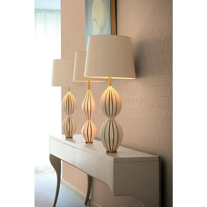 A.S. Création Jade 2 Vliestapete - Altrosa-Gold, Grafisch, 10,05 x 0,53 m - Drei dekorative Tischlampen mit cremefarbenen Schirmen stehen auf einem weißen Konsolentisch vor einer gemusterten Wand.