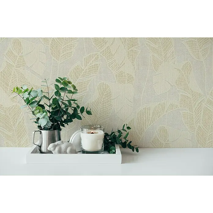 A.S. Création Jade 2 Vliestapete Blätter - Weiß-Beige-Gold, Floral, 10,05 x 0,53 m - Stillleben mit Zimmerpflanzen, Kerze und Dekoration auf einem weißen Tablett vor einer beigen Blättertapete.