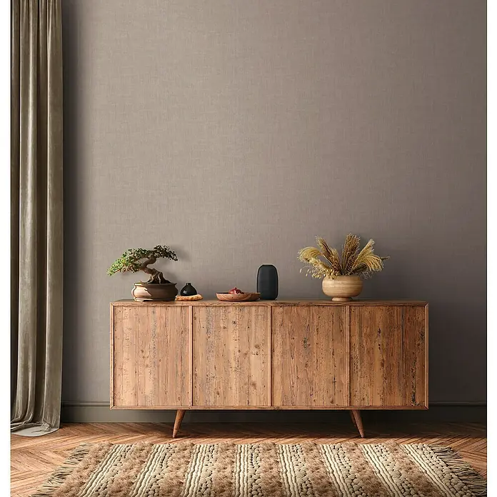 A.S. Création Jade 2 Vliestapete - Braungrau, Uni, 10,05 x 0,53 m - Ein rustikales Holzsideboard mit dekorativen Elementen wie Bonsai und Vasen, ergänzt durch einen Teppich und Vorhänge.