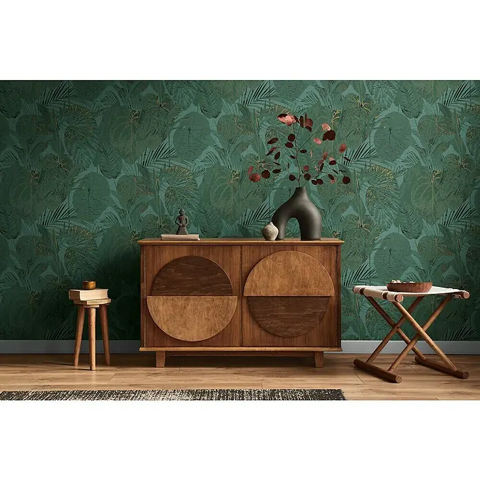 A.S. Création Famous Garden Vliestapete Dschungel - Petrol-Grün-Gold, Floral, 10,05 x 0,53 m - Einrichtung mit einem hölzernen Sideboard, Hockern und einer grünen Blättertapete.