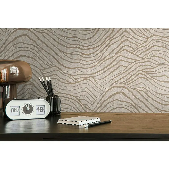 A.S. Création Jade 2 Vliestapete - Beige-Gold-Grau, 3D-Optik, 10,05 x 0,53 m - Nahaufnahme eines Tisches mit einer Retro-Flip-Uhr, Stiften und einem Notizbuch vor einer gemusterten Tapete.