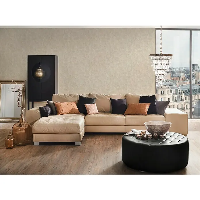 A.S. Création Jade 2 Vliestapete - Beige, Uni, 10,05 x 0,53 m - Wohnzimmer mit beigem Ledersofa, schwarzen Zierkissen und einem schwarzen, runden Couchtisch mit Dekorationen. Elegante Atmosphäre.