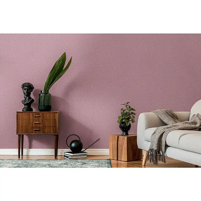 A.S. Création Famous Garden Vliestapete - Violett-Pink, Uni, 10,05 x 0,53 m - Elegantes Interieur mit einem grauen Sofa, einem Holztisch, einer Kommode und dekorativen Accessoires wie Pflanzen und einer Skulptur.