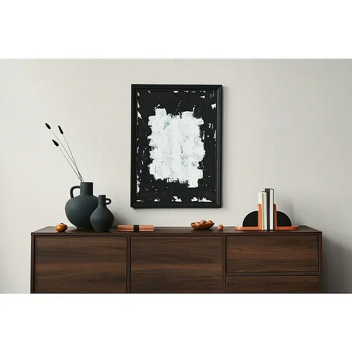 A.S. Création Famous Garden Vliestapete - Creme-Weiß, Uni, 10,05 x 0,53 m - Abstraktes Kunstwerk in Schwarz und Weiß, gerahmt und an einer Wand über einem dunklen Holzschrank platziert, das eine moderne Atmosphäre schafft.