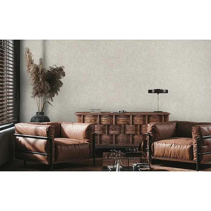 A.S. Création Stories of Life Vliestapete Used-Look - Beige-Silber, Betonoptik, 10,05 x 0,53 m - Wohnzimmer mit zwei braunen Sesseln aus Leder, einem Lowboard aus Holz und einem kleinen Tisch aus Glas.
