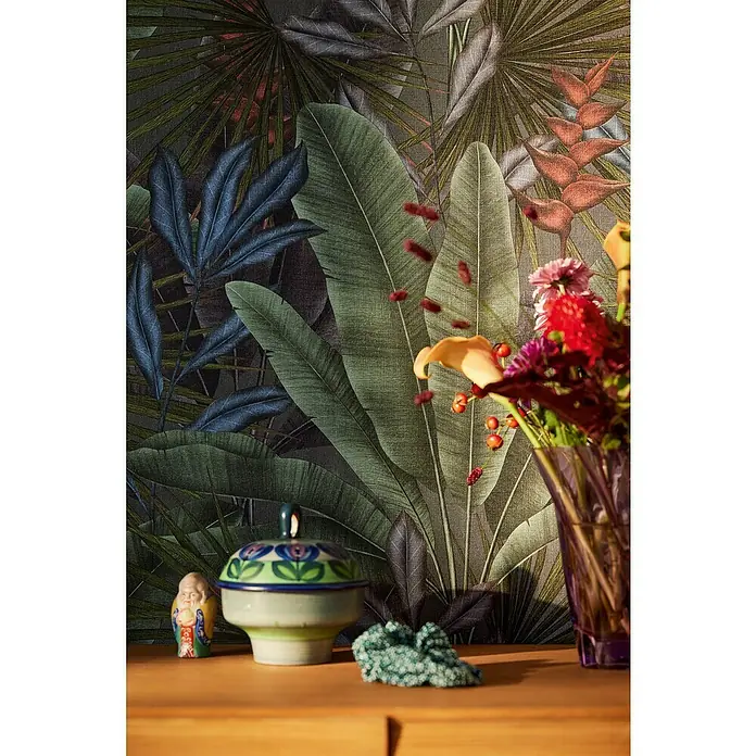 A.S. Création Stories of Life Vliestapete - Grau-Grün-Rot, Floral, 10,05 x 0,53 m - Dekoratives Stillleben mit Blumenvase, Keramikdose und Buddha-Figur auf einer Holzkommode vor tropischer Blättertapete.