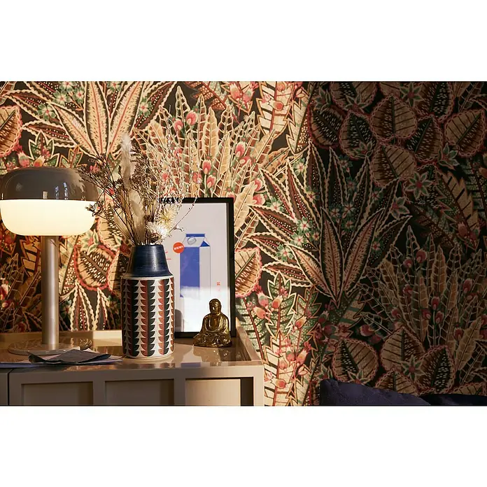A.S. Création Stories of Life Vliestapete Blumen - Braun-Rot-Schwarz, Floral, 10,05 x 0,53 m - Elegante Tischlampe mit einem milchglasartigen Schirm, kombiniert mit einer dekorativen Blumenvase und einer Buddha-Statue auf einem stilvollen Beistelltisch.
