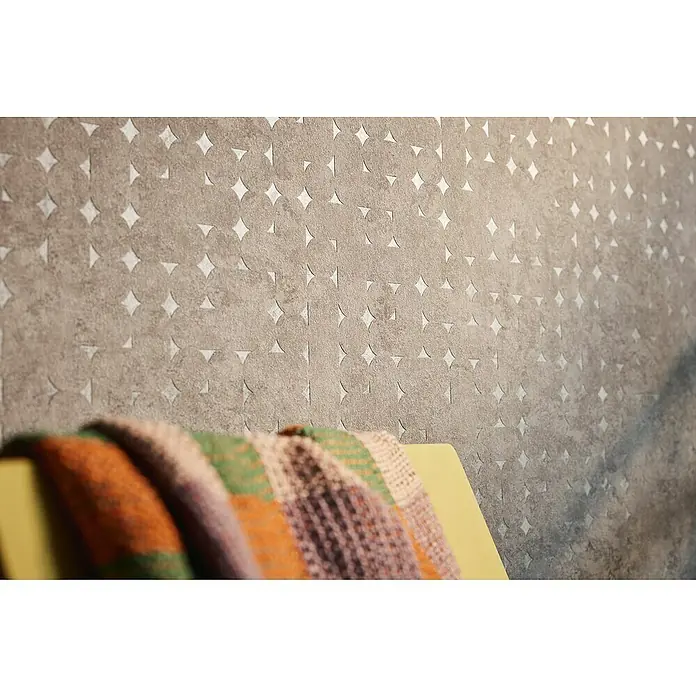A.S. Création Stories of Life Vliestapete Used-Look - Beige-Braun, Betonoptik, 10,05 x 0,53 m - Nahaufnahme einer strukturierten, grauen Wand mit einem Muster aus Kreisen und Rauten, die eine subtile und moderne Ästhetik verleiht.