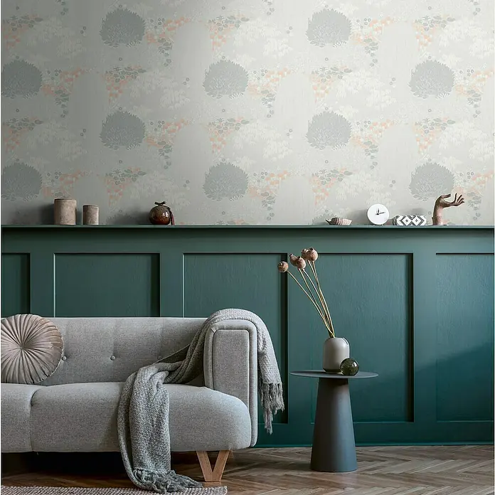 A.S. Création Famous Garden Vliestapete - Hellgrau-Weiß-Rosa, Floral, 10,05 x 0,53 m - Elegante Wandgestaltung mit floralem Tapetenmuster in sanften Farben über einer grünen Wandvertäfelung und einem stilvollen grauen Sofa.