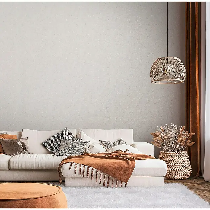 A.S. Création Stories of Life Vliestapete Used-Look - Beige-Silber, Betonoptik, 10,05 x 0,53 m - Wohnzimmer-Szene mit stilvoller Lampe, Sofa, Kissen, Decke und Teppich für ein gemütliches Ambiente.