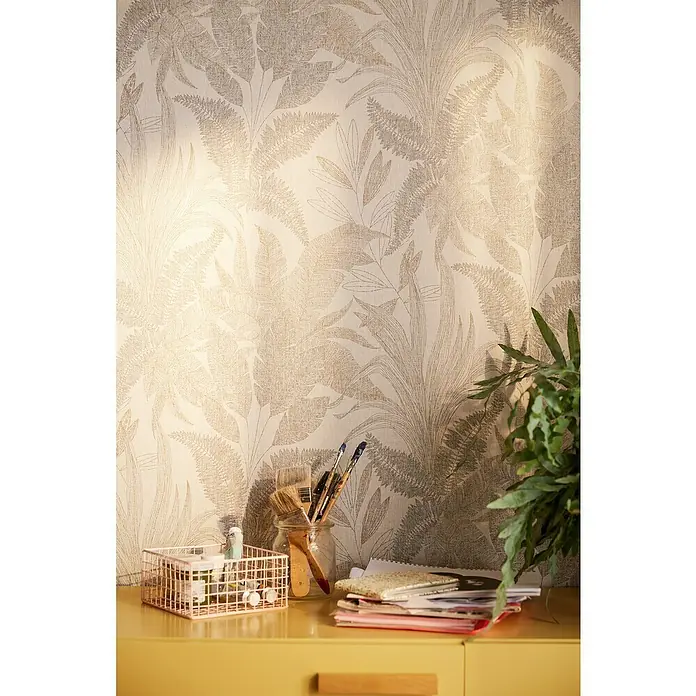 A.S. Création Stories of Life Vliestapete Dschungel - Beige-Gold, Floral, 10,05 x 0,53 m - Nahaufnahme von Pinseln im Glas, Aufbewahrungskorb und Notizbüchern auf einem gelben Tisch vor einer floralen Tapete.