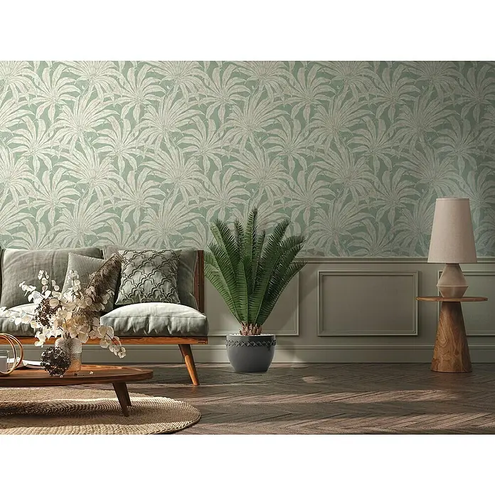 A.S. Création Jade 2 Vliestapete Pflanzen - Grün-Gold-Silber, Floral, 10,05 x 0,53 m - Wohnzimmer mit Couch, Tischlampe und Pflanze vor einer botanischen Tapete mit Blättern.