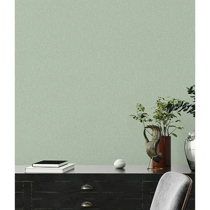 A.S. Création Famous Garden Vliestapete - Grün, Uni, 10,05 x 0,53 m - Nahaufnahme eines eleganten Arbeitsbereichs mit einem dunklen Holzschrank, Büchern, Pflanzen und dekorativen Elementen vor einer mintfarbenen Wand.