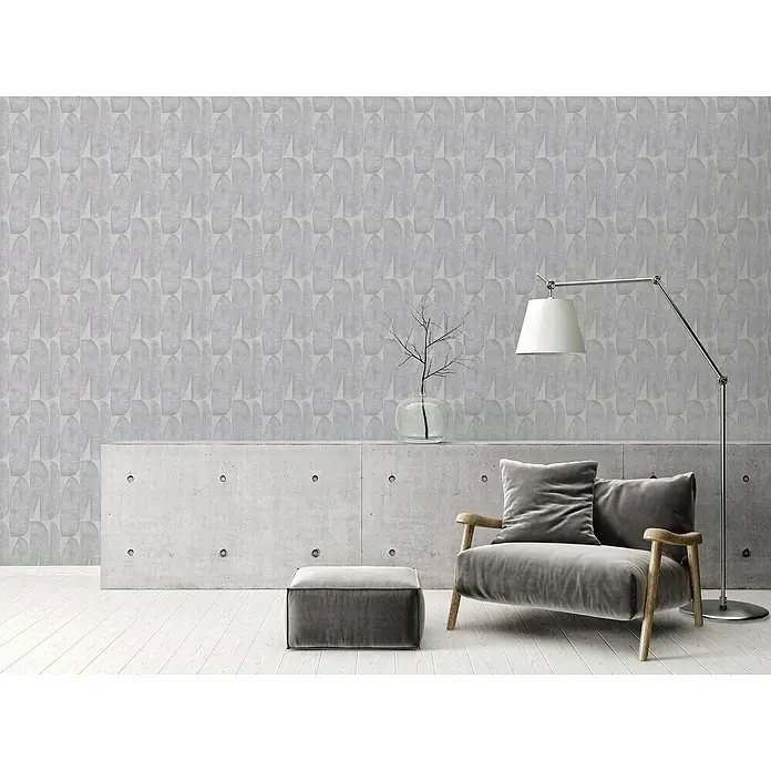 A.S. Création Stories of Life Vliestapete - Helles Braungrau, Floral, 10,05 x 0,53 m - Einrichtungsidee mit einem modernen grauen Sessel mit Ottomane, Stehlampe und einer stilvollen Betonkommode vor einer gemusterten Tapete.
