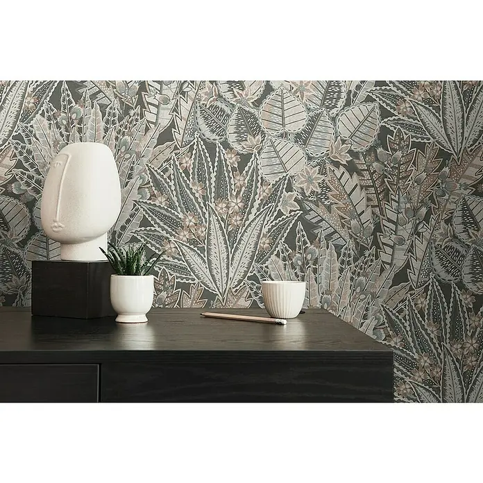 A.S. Création Stories of Life Vliestapete Blumen - Schwarz-Braun-Grau, Floral, 10,05 x 0,53 m - Nahaufnahme von Dekorationsartikeln wie eine Skulptur, eine Pflanze, eine Tasse und ein Bleistift auf einem dunklen Tisch mit floralem Hintergrund.