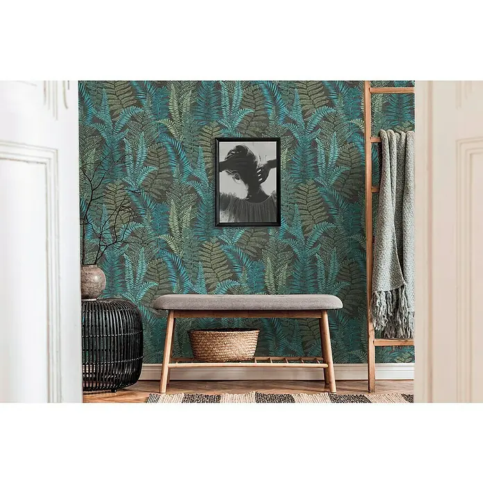 A.S. Création Famous Garden Vliestapete - Schwarz-Blau-Grün, Floral, 10,05 x 0,53 m - Einrichtungsidee mit einem Hocker mit grauem Polster vor einer Wand mit Farnmotivtapete, darüber ein gerahmtes Bild, daneben eine Leiter mit Decke.