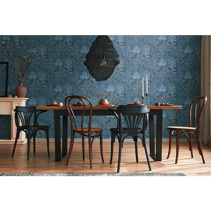 A.S. Création Famous Garden Vliestapete - Blau-Weiß-Grau, Floral, 10,05 x 0,53 m - Holztisch mit verschiedenen Stühlen, darunter zwei schwarze und zwei braune Bugholzstühle, unter einer auffälligen Hängelampe.