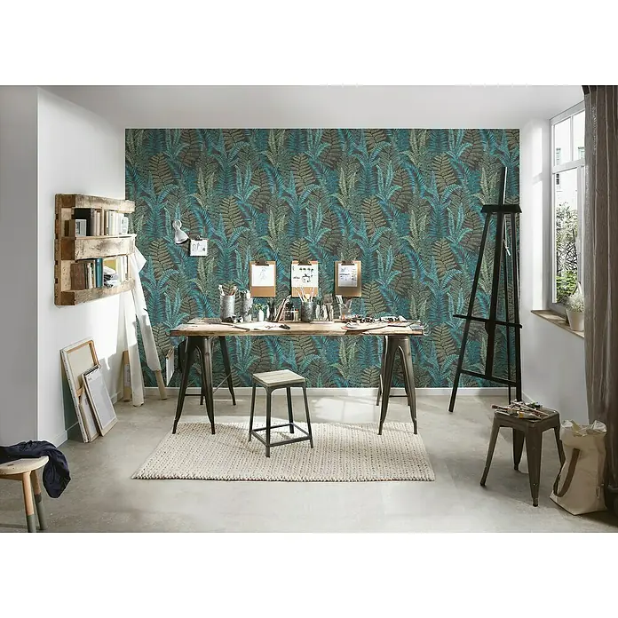 A.S. Création Famous Garden Vliestapete - Schwarz-Blau-Grün, Floral, 10,05 x 0,53 m - Das Bild zeigt ein Atelier mit einer grünen Tapete mit Farnmuster, einem Holztisch mit Metallbeinen, einer Staffelei und diversen Kunstutensilien.