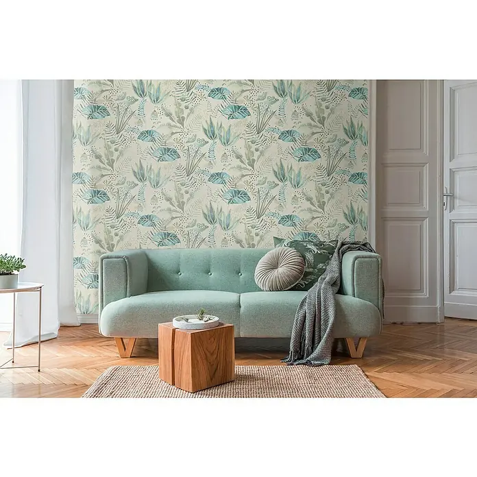 A.S. Création Famous Garden Vliestapete - Beige-Grün-Blau, Floral, 10,05 x 0,53 m - Gemütliches Wohnzimmer mit mintgrünem Sofa vor einer botanischen Tapete, ergänzt durch einen Holzhocker und einen Teppich.