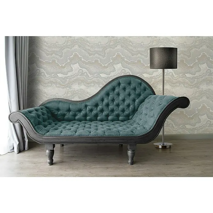 A.S. Création Stories of Life Vliestapete Marmoroptik Metallic-Effekt - Grau-Silber-Gold, Steinoptik, 10,05 x 0,53 m - Elegante Chaiselongue mit dunkelgrünem Samtbezug und Knopfheftung vor einer gemusterten Wand und einer Stehlampe.