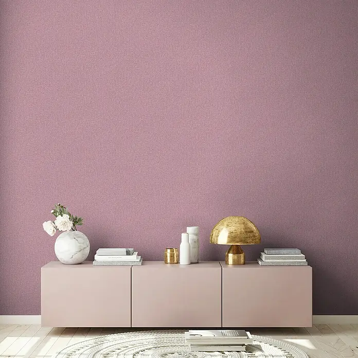 A.S. Création Famous Garden Vliestapete - Violett-Pink, Uni, 10,05 x 0,53 m - Wohnzimmer Interieur mit einer hellrosa Kommode, einer goldenen Lampe und dekorativen Elementen vor einer lila Wand.