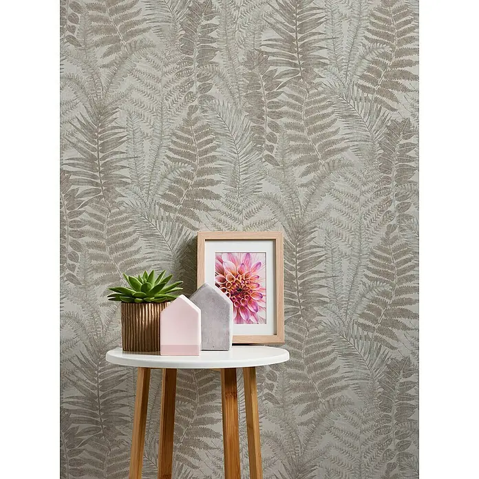 A.S. Création Famous Garden Vliestapete - Grau-Beige-Taupe, Floral, 10,05 x 0,53 m - Nahaufnahme eines dekorierten Beistelltisches mit Topfpflanze, Zierhäusern und einem gerahmten Bild auf einem stilvollen Wandhintergrund.