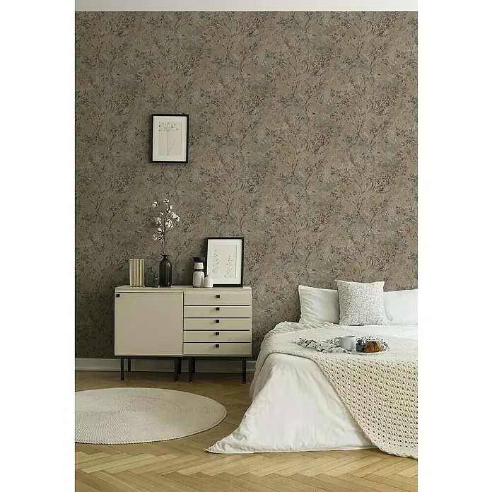 A.S. Création Stories of Life Vliestapete Zweig - Braun-Grau-Gold, Floral, 10,05 x 0,53 m - Ein Schlafzimmer mit einer gemusterten Tapete in Braun- und Grautönen, einem hellen Nachttisch und einem Bett mit weißer Bettwäsche.