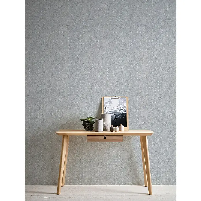 A.S. Création Stories of Life Vliestapete Used-Look - Betongrau-Silber, Betonoptik, 10,05 x 0,53 m - Minimalistischer Schreibtisch aus hellem Holz mit Dekorationen vor einer grauen Wand.