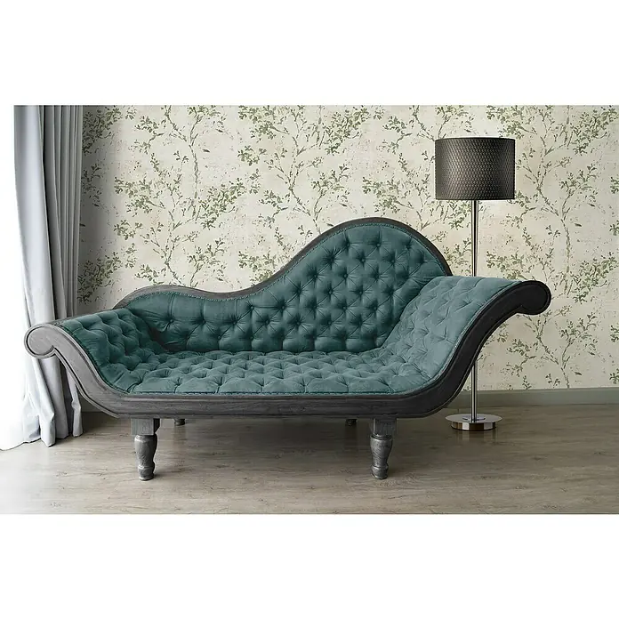 A.S. Création Stories of Life Vliestapete Zweig - Beige-Grün-Gold, Floral, 10,05 x 0,53 m - Elegante graugrüne Chaiselongue mit Knopfheftung und geschwungenem Rahmen vor einer floralen Tapete, ergänzt durch eine Stehlampe.