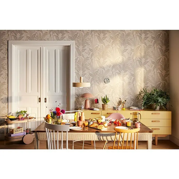 A.S. Création Stories of Life Vliestapete Dschungel - Beige-Gold, Floral, 10,05 x 0,53 m - Frühstückstisch mit Speisen und Getränken, umgeben von Stühlen und einem Beistelltisch, vor einer floralen Tapete und einer gelben Kommode.