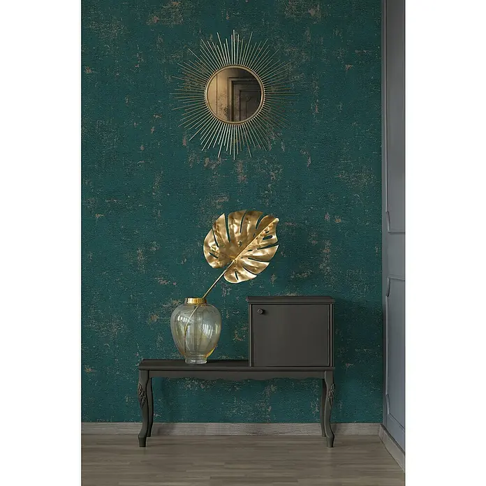 A.S. Création Jade 2 Vliestapete - Petrol-Gold, Uni, 10,05 x 0,53 m - Stilvolles Interieur mit einem Spiegel im Sonnenstil, einer goldenen Monstera-Pflanze in einer Vase und einem dunklen Sideboard auf einem dekorierten Tisch.