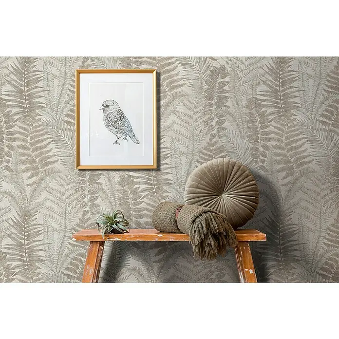 A.S. Création Famous Garden Vliestapete - Grau-Beige-Taupe, Floral, 10,05 x 0,53 m - Dekorative Nahaufnahme eines Zimmers mit einem gerahmten Vogelbild, einer Pflanze und einem runden Kissen auf einem Beistelltisch vor einer botanischen Tapete.