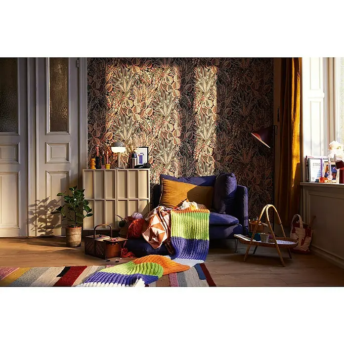 A.S. Création Stories of Life Vliestapete Blumen - Braun-Rot-Schwarz, Floral, 10,05 x 0,53 m - Gemütliches Wohnzimmer mit einem blauen Sessel, einem bunten Teppich und einer dekorativen Tapete.