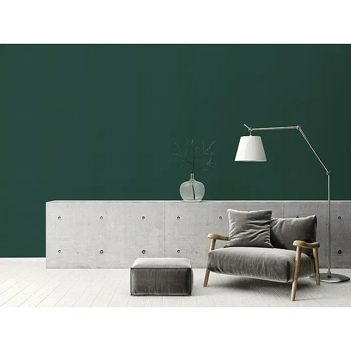 A.S. Création Stories of Life Vliestapete - Grün-Dunkelgrün, Uni, 10,05 x 0,53 m - Eine stilvolle Wohnzimmerszene mit einem modernen Sessel aus grauem Samt, einer eleganten Stehlampe und einem minimalistischen Betonsockel.