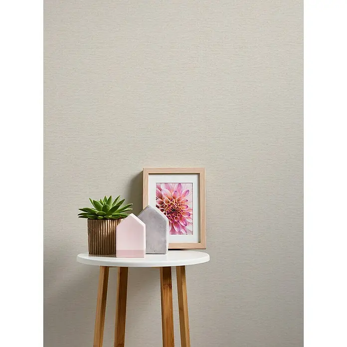 A.S. Création Famous Garden Vliestapete - Creme-Weiß-Beige, Uni, 10,05 x 0,53 m - Nahaufnahme eines stilvollen Beistelltisches mit Sukkulente, Deko-Häusern und gerahmtem Blumendruck, der moderne Ästhetik und natürliche Elemente vereint.