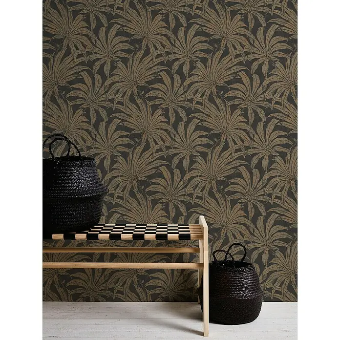 A.S. Création Jade 2 Vliestapete Pflanzen - Schwarz-Gold-Bronze, Floral, 10,05 x 0,53 m - Einrichtungsszene mit einem hölzernen Hocker, zwei schwarzen Körben und einer Wand mit Pflanzenmustertapete.