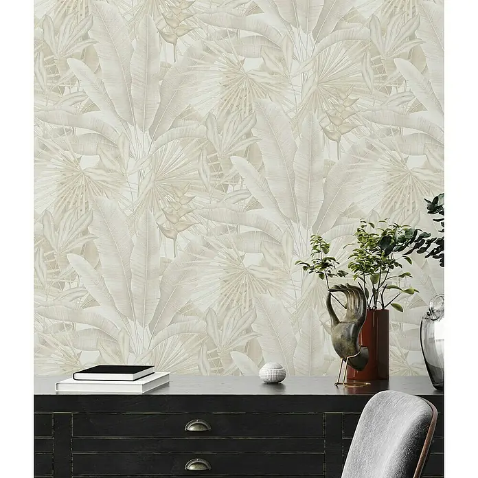 A.S. Création Stories of Life Vliestapete - Beige-Creme-Grau, Floral, 10,05 x 0,53 m - Zimmer mit tropischem Blättertapetenmuster, einer Kommode mit Dekoration und einem grauen Stuhl.