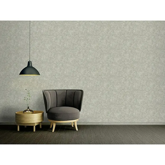 A.S. Création Stories of Life Vliestapete Used-Look - Betongrau-Grün, Betonoptik, 10,05 x 0,53 m - Grauer Sessel auf Holzboden neben rundem Tisch mit Lampe. Elegantes Möbelstück für Wohnzimmer mit stilvollem Design.
